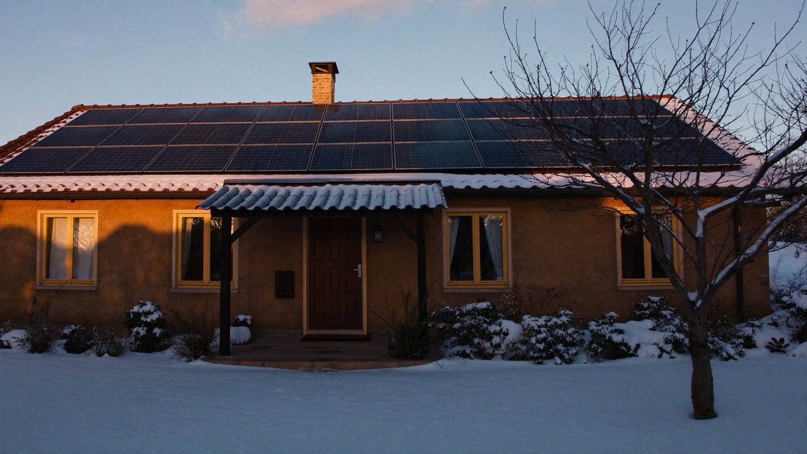 Kuća sa solarnom elektranom u snijegu u sumrak – dizalica topline i solarna elektrana zimi